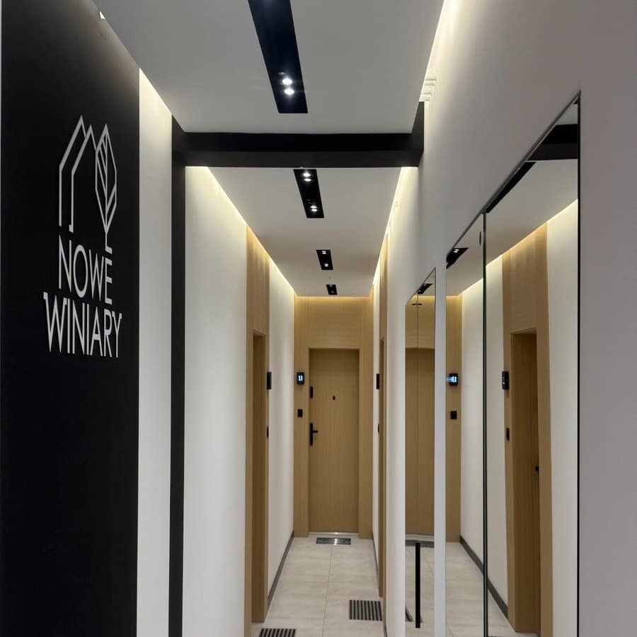 Korytarz z logo Nowe Winiary na ścianie i drzwiami do mieszkań